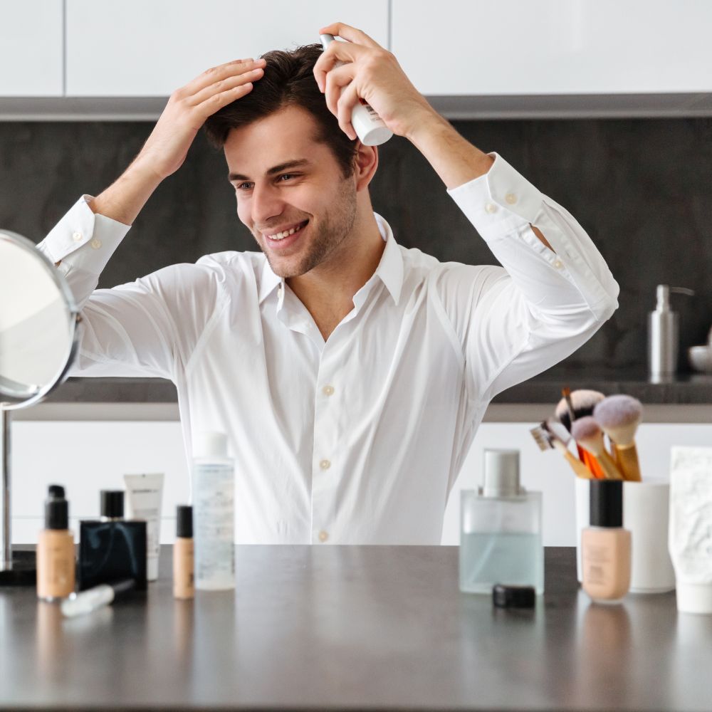 Smiling man spraying hair product while looking in vanity mirror