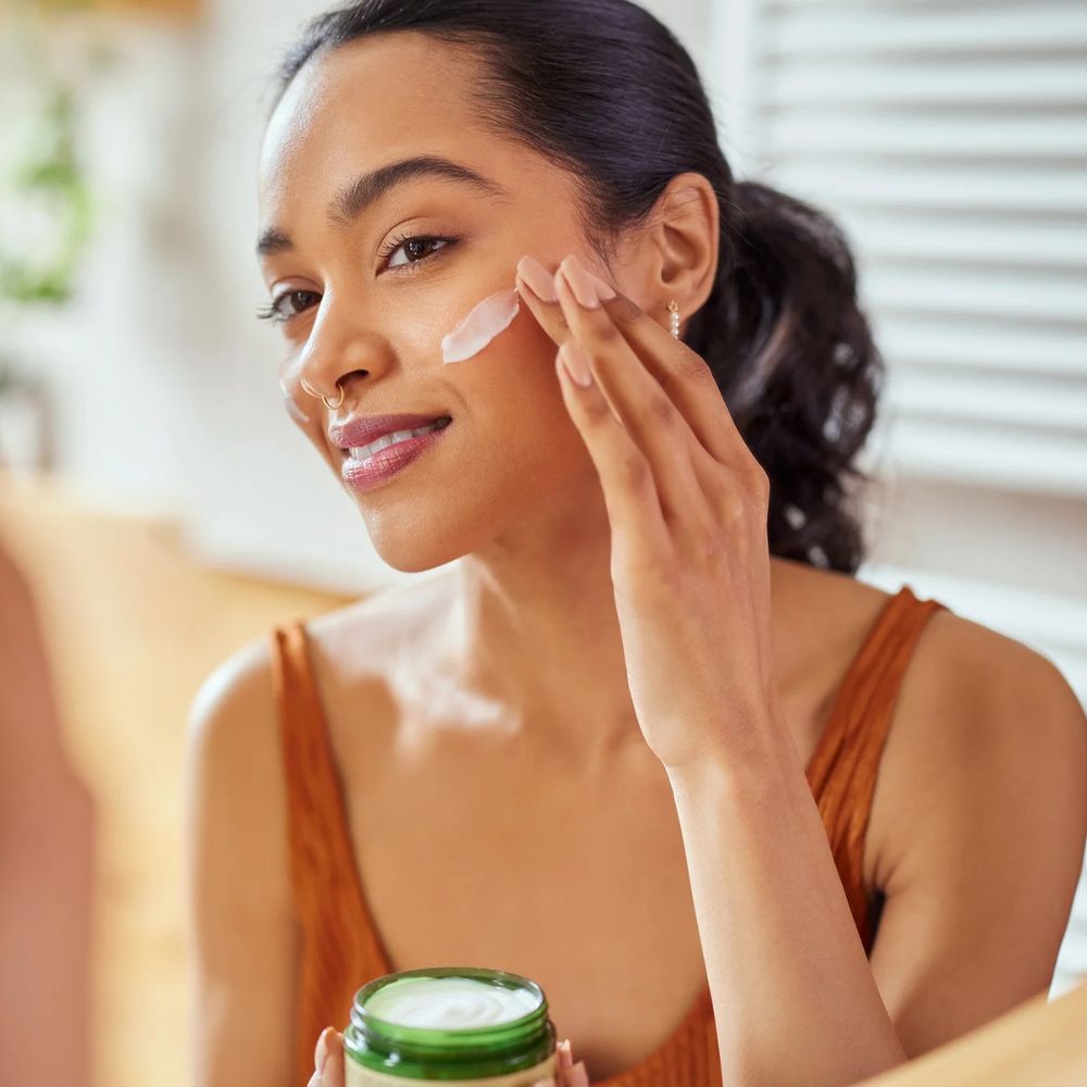 Young woman applying white moisturizer cream on her cheek